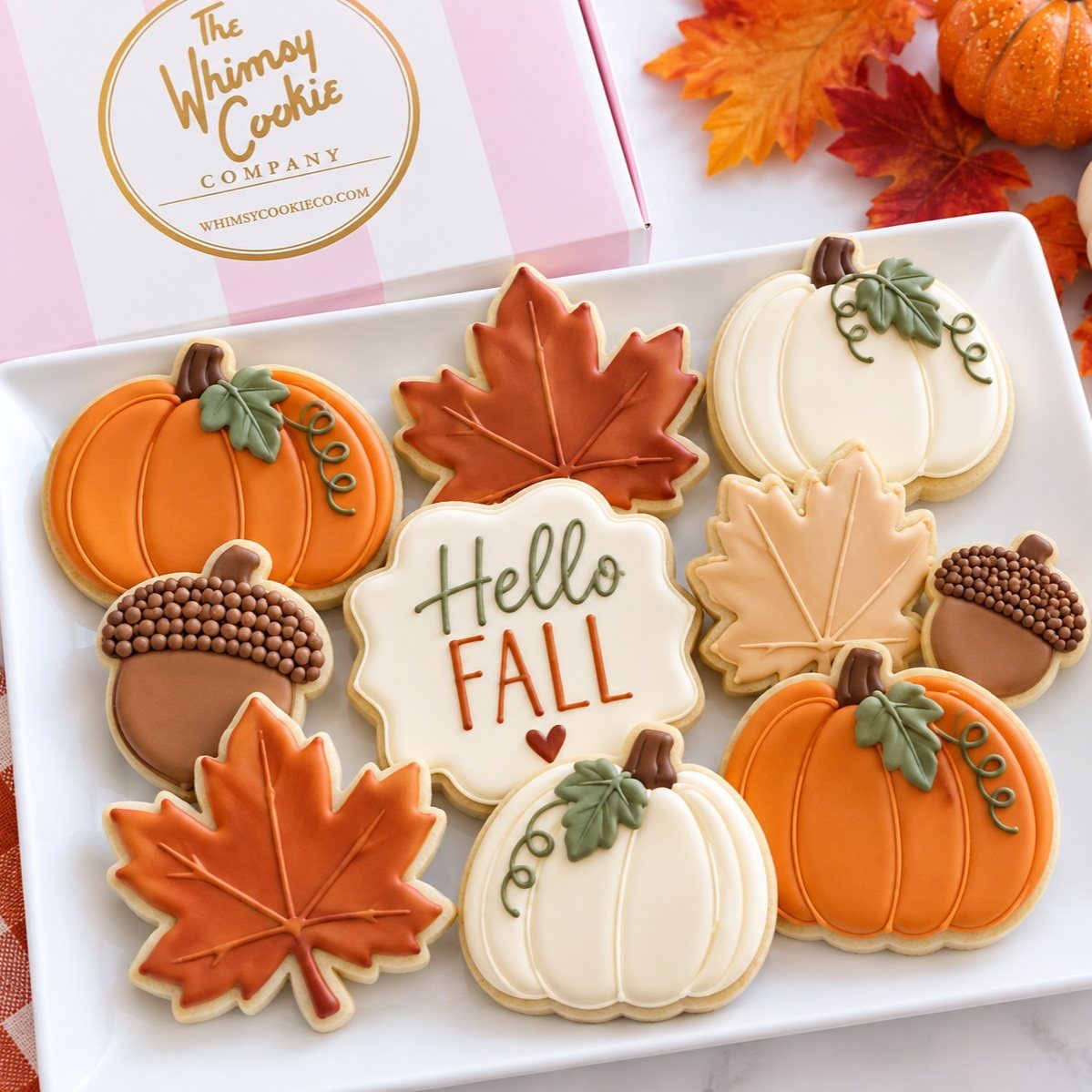 Iced sugar cookies shaped like pumpkins, leaves, and acorns on a white platter.