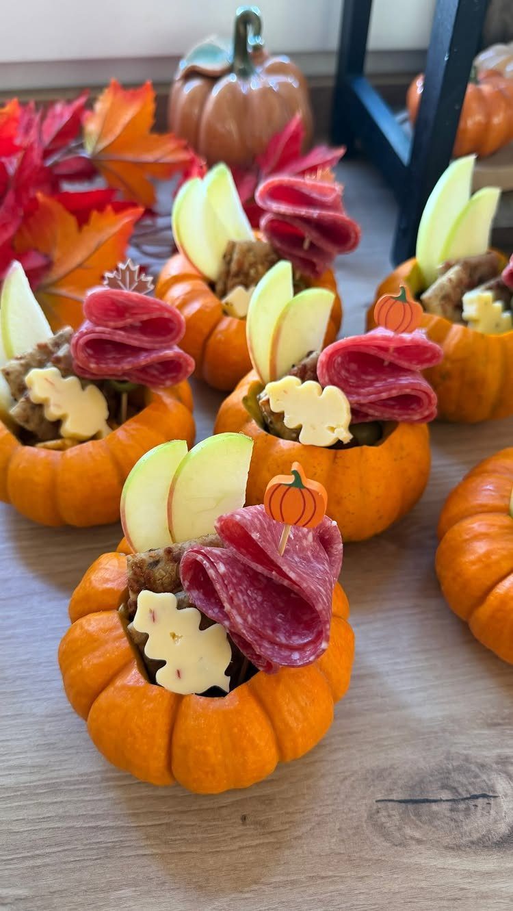 Mini pumpkins filled with salami, apple slices, and cheese on a wooden table.