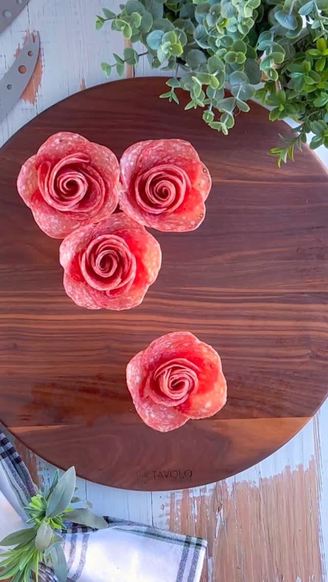Salami rolled into rose shapes on a round dark wooden serving board.