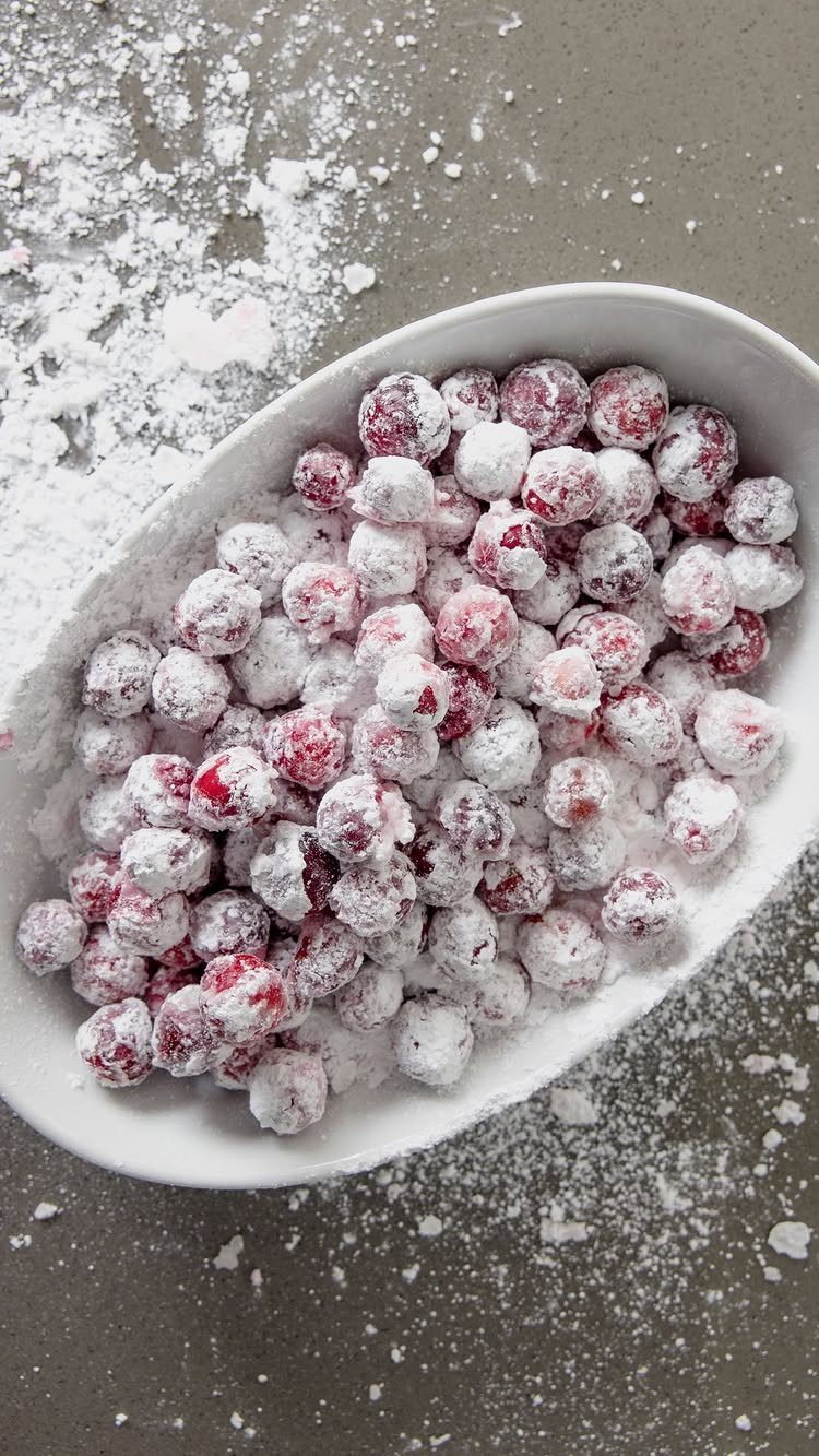 Powdered sugar coated cranberries in a white oval bowl on grey background