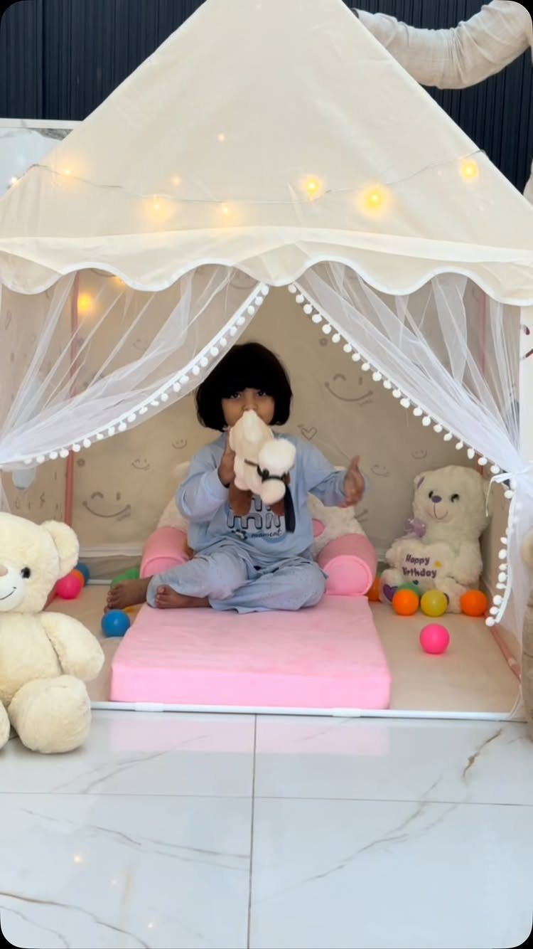 Child sitting inside a white fabric play tent with plush toys and lights