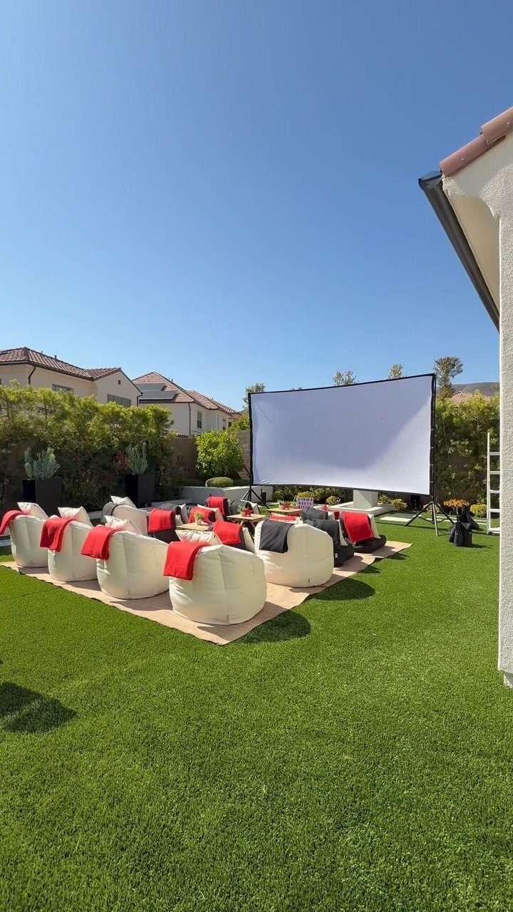 Outdoor movie screen with white bean bag chairs and red blankets on grass