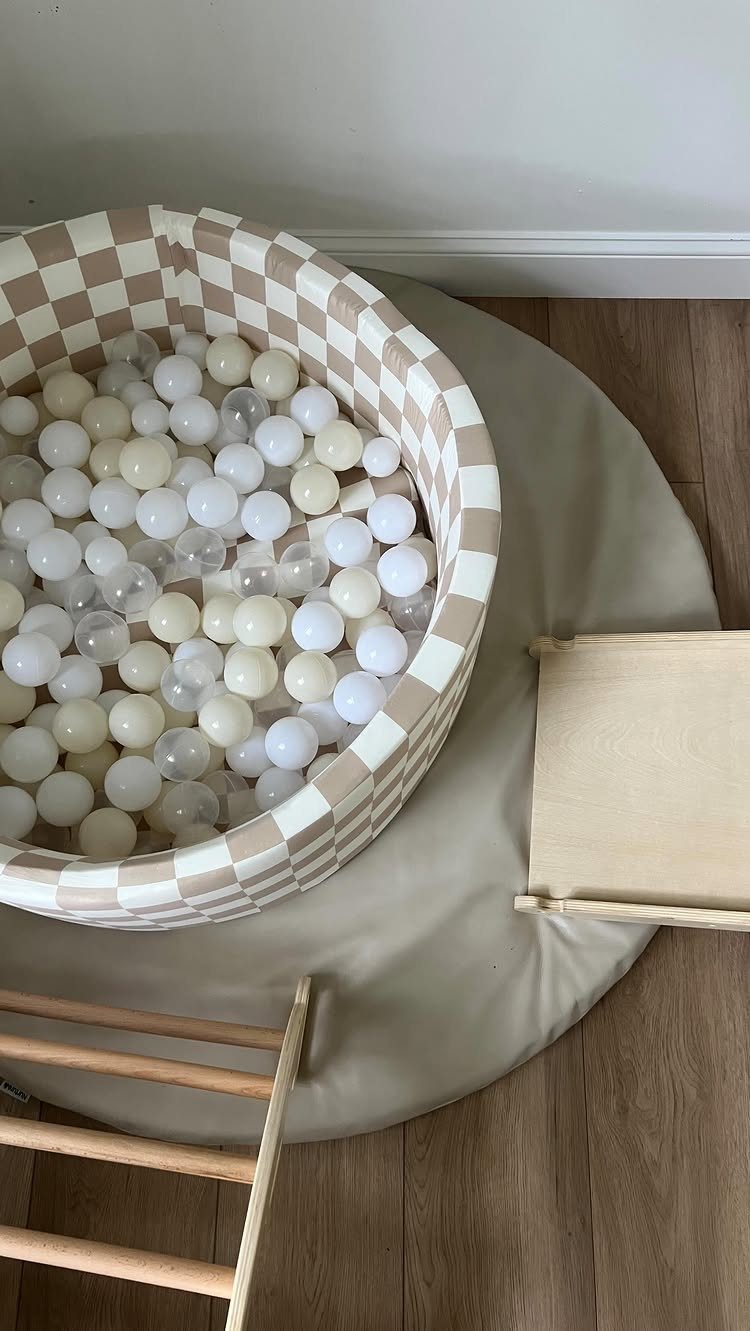 Checkered ball pit filled with white balls on a beige mat and wooden floor