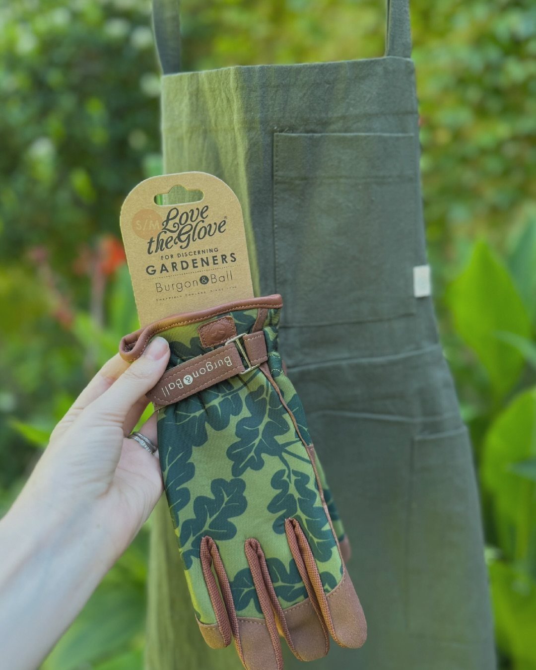 Green leaf-patterned gardening glove with leather accents held against a green apron.
