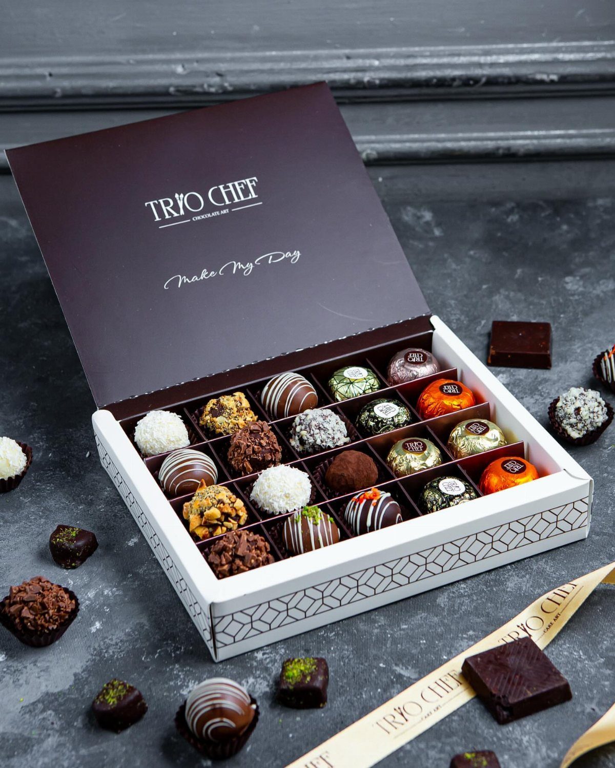 Assorted gourmet chocolate truffles in a white patterned box on a grey surface.