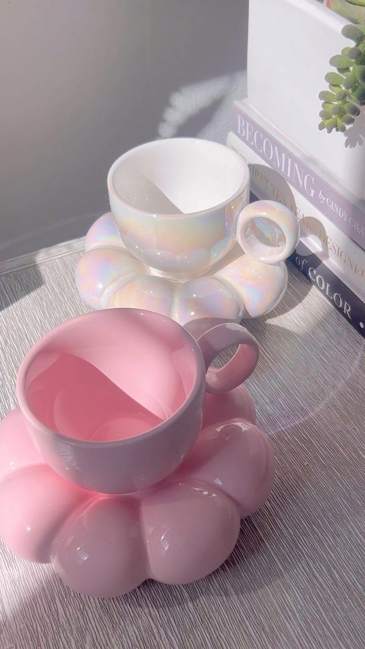 Two ceramic coffee cups on cloud-shaped saucers in iridescent white and pastel pink.