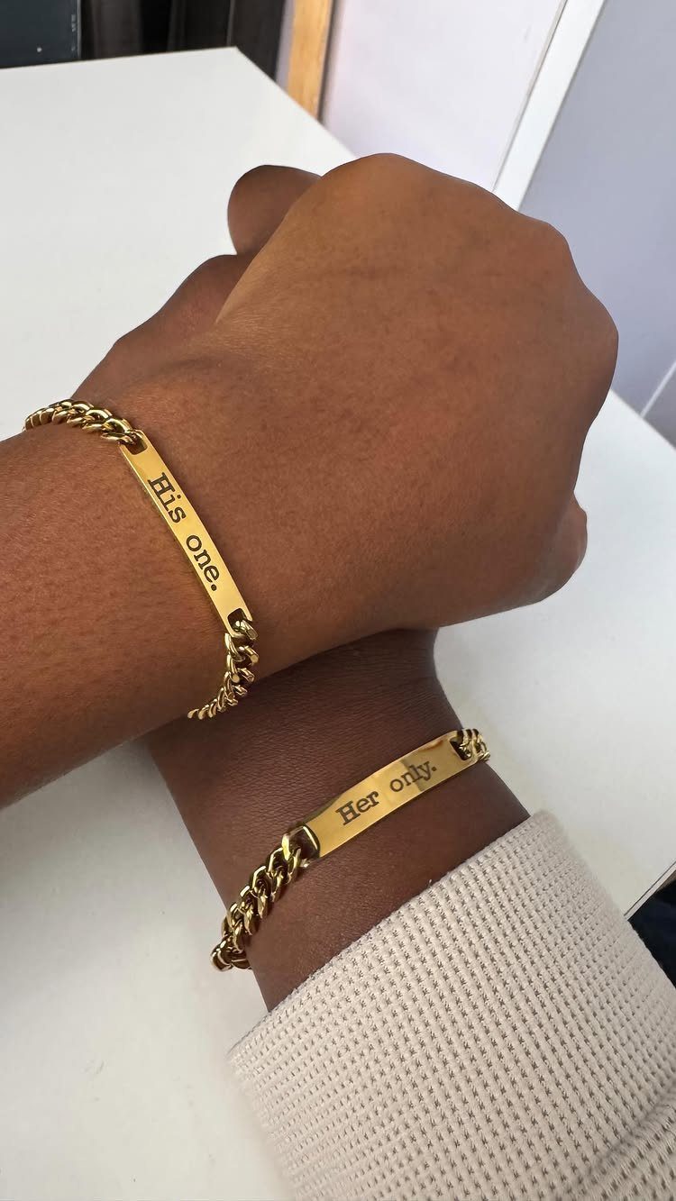Matching gold chain bracelets on two wrists with His one and Her only engravings