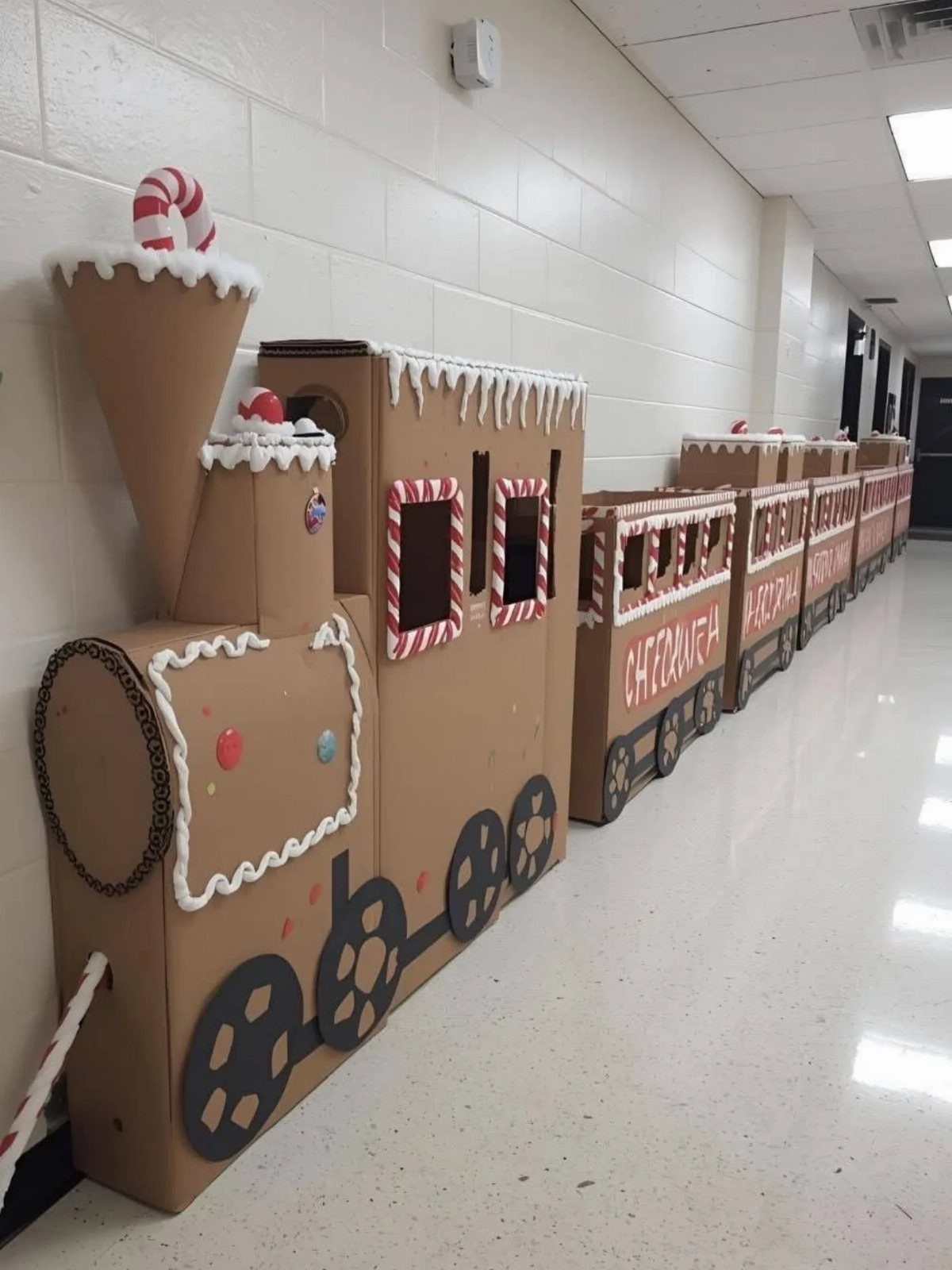 Cardboard box train decorated for Christmas in a white school hallway.