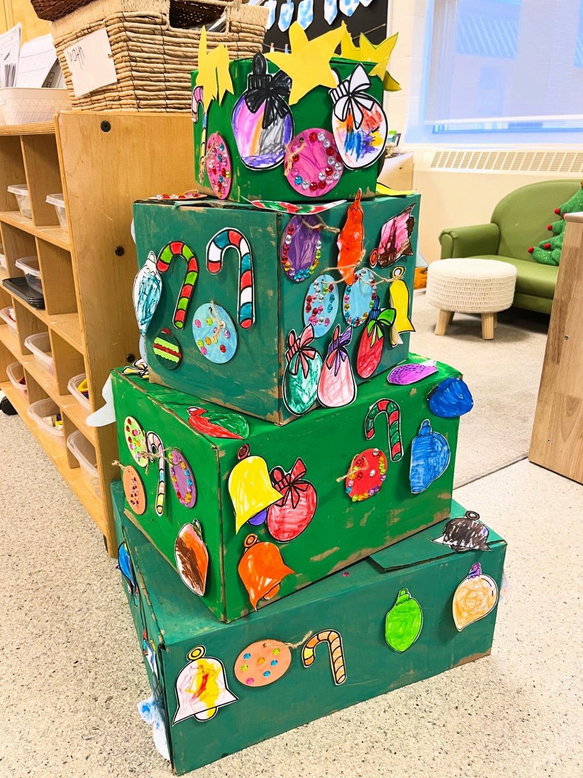Green painted cardboard boxes stacked as a Christmas tree with colorful paper ornaments.