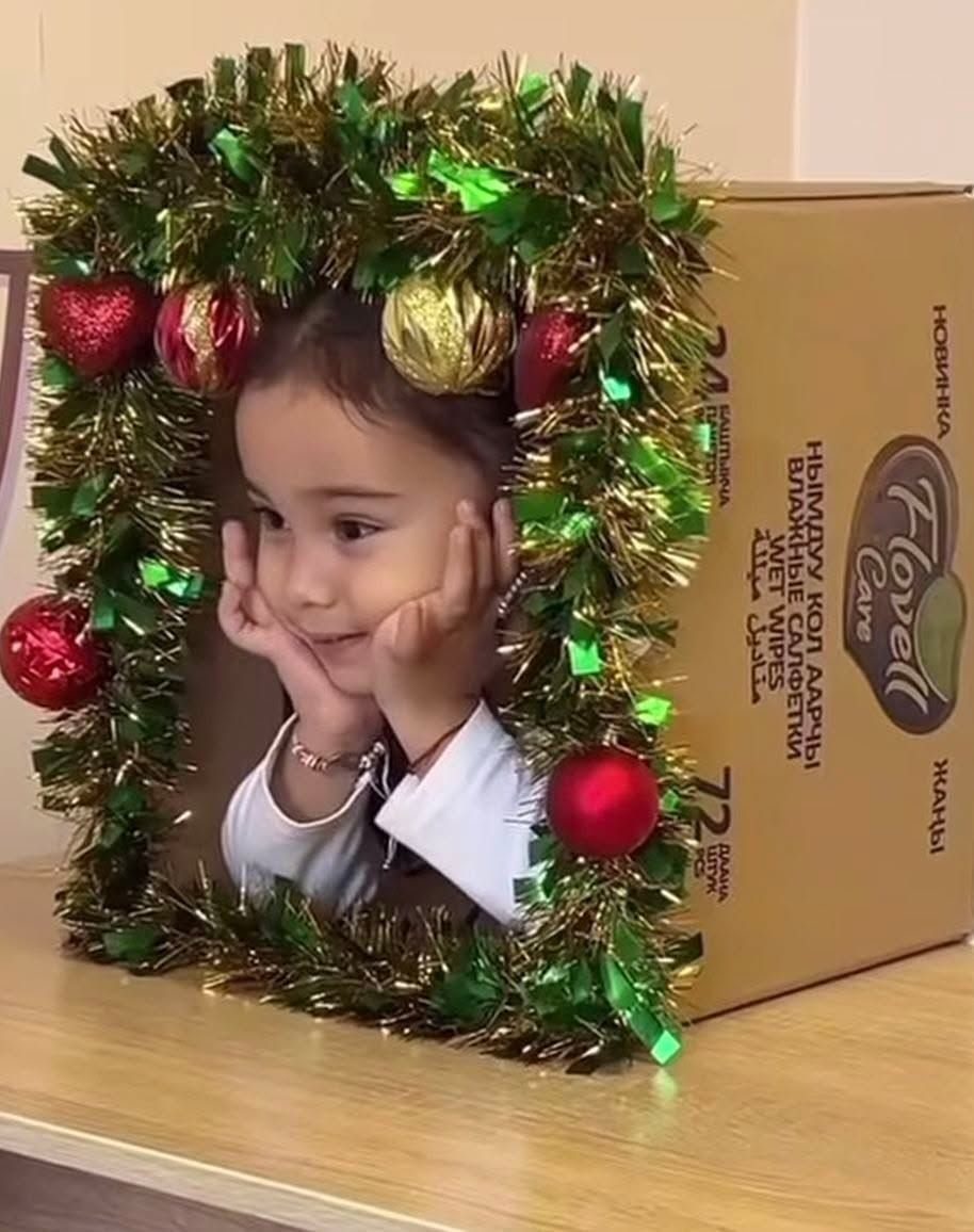 Young girl posing inside a cardboard box decorated with festive Christmas tinsel and ornaments