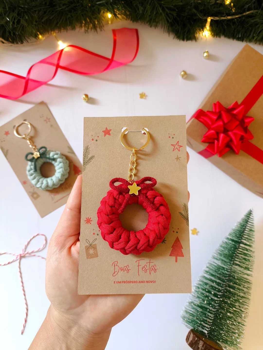 Red crocheted wreath keychain on a cardboard tag held by a hand.
