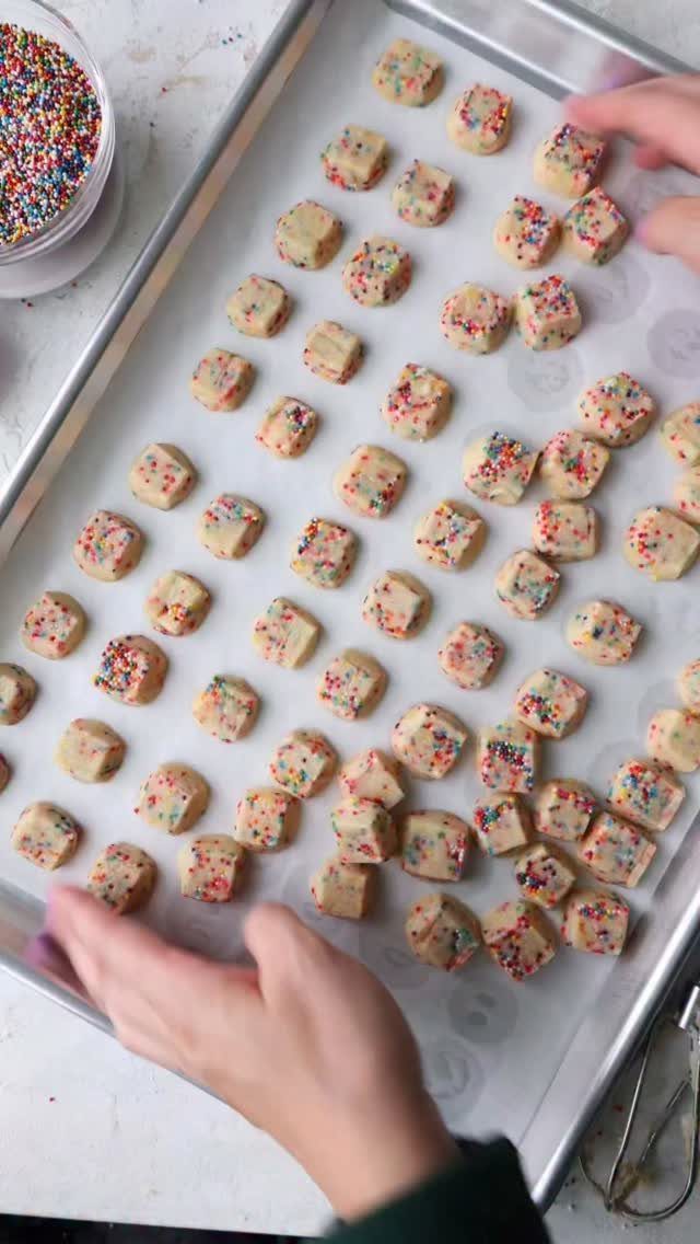 Square cookie dough pieces with rainbow sprinkles on a baking sheet.