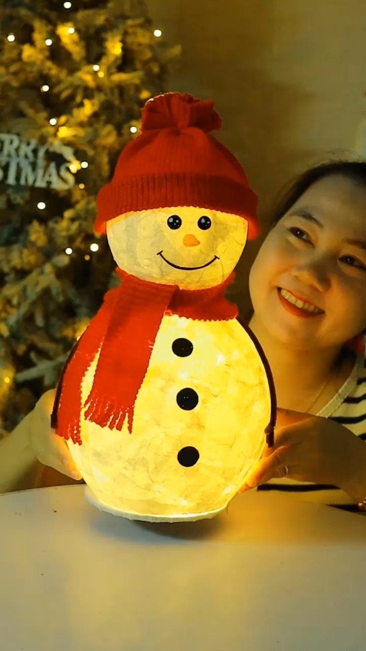 Glowing handmade snowman lamp with red hat and scarf held by a woman.