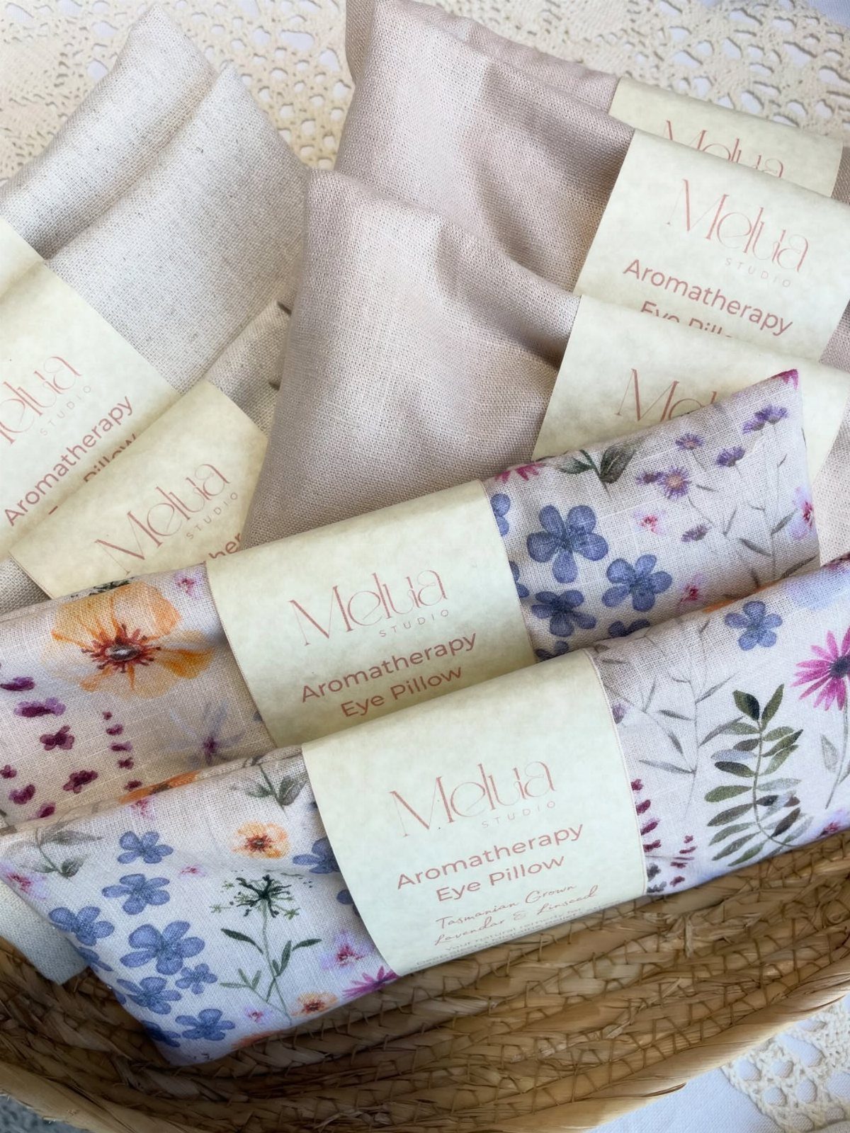 Fabric aromatherapy eye pillows with floral patterns and labels in a woven basket.