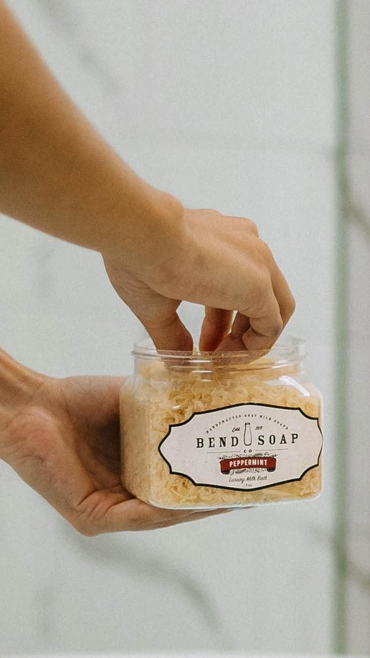 Hands holding a glass jar of peppermint milk bath with a white label.