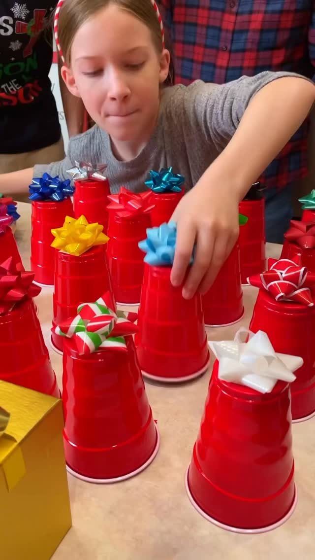 Girl playing a game with red plastic cups topped with colorful gift bows.
