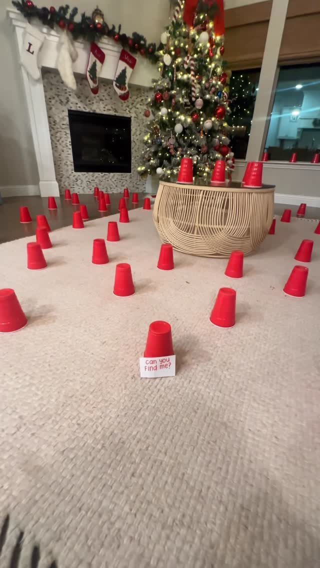 Red plastic cups scattered on a carpet near a decorated Christmas tree and fireplace.