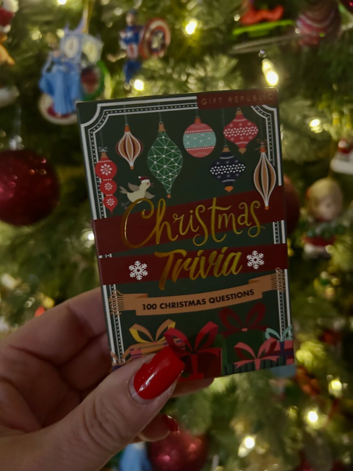 Christmas Trivia card game box held in front of a decorated holiday tree