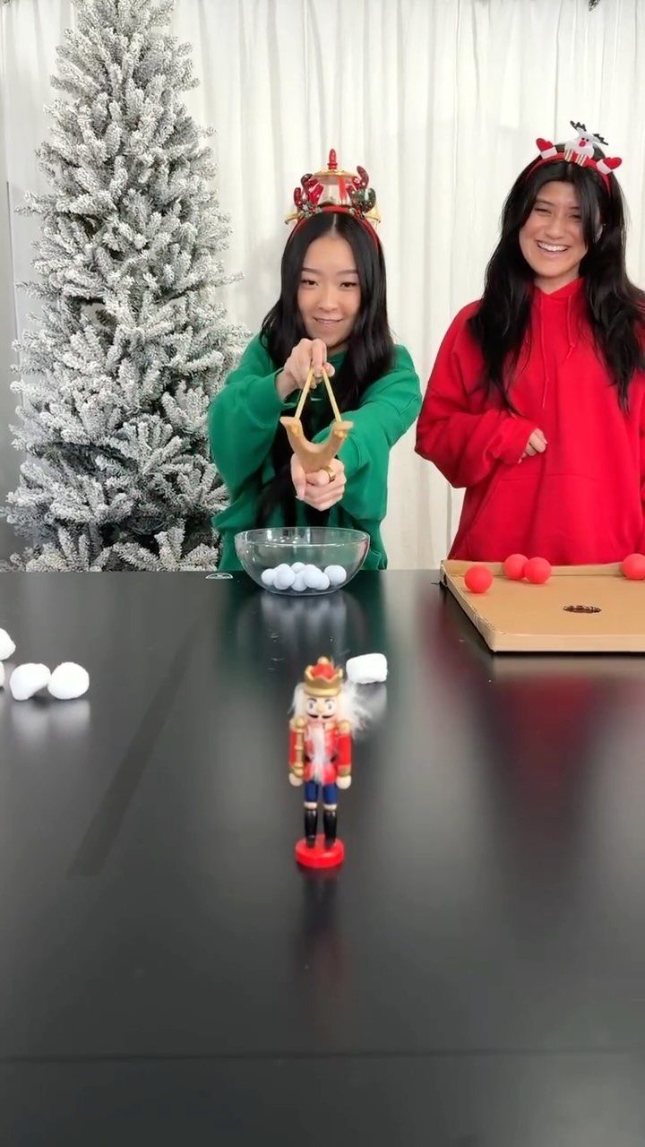 Woman in green sweater using a slingshot to launch pom-poms at a nutcracker.