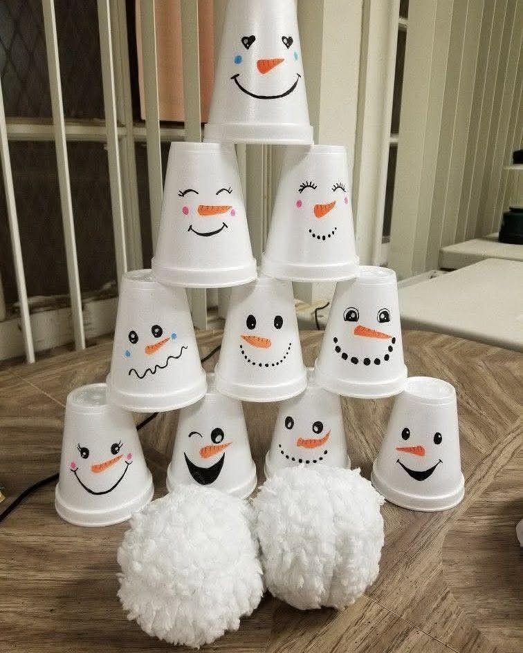 Snowman faces drawn on white plastic cups stacked for a holiday bowling game.