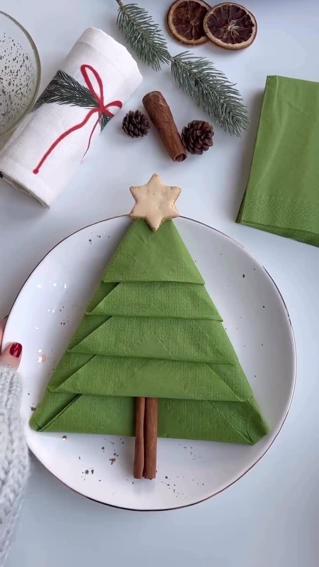 Green napkin folded as a Christmas tree on a white plate with festive decorations