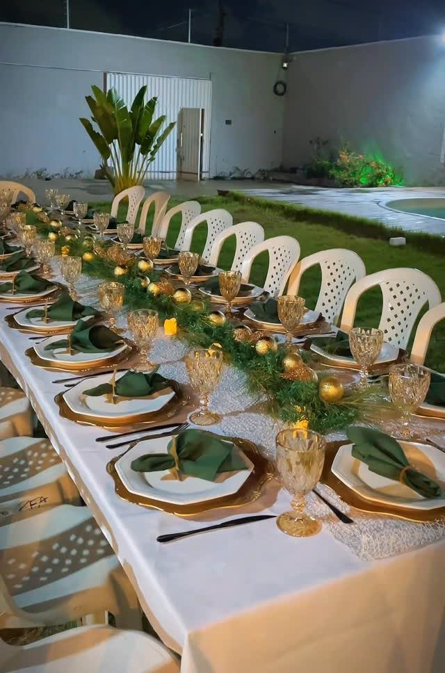 Long outdoor dinner table with white tablecloth, gold plates, and evergreen greenery runner.