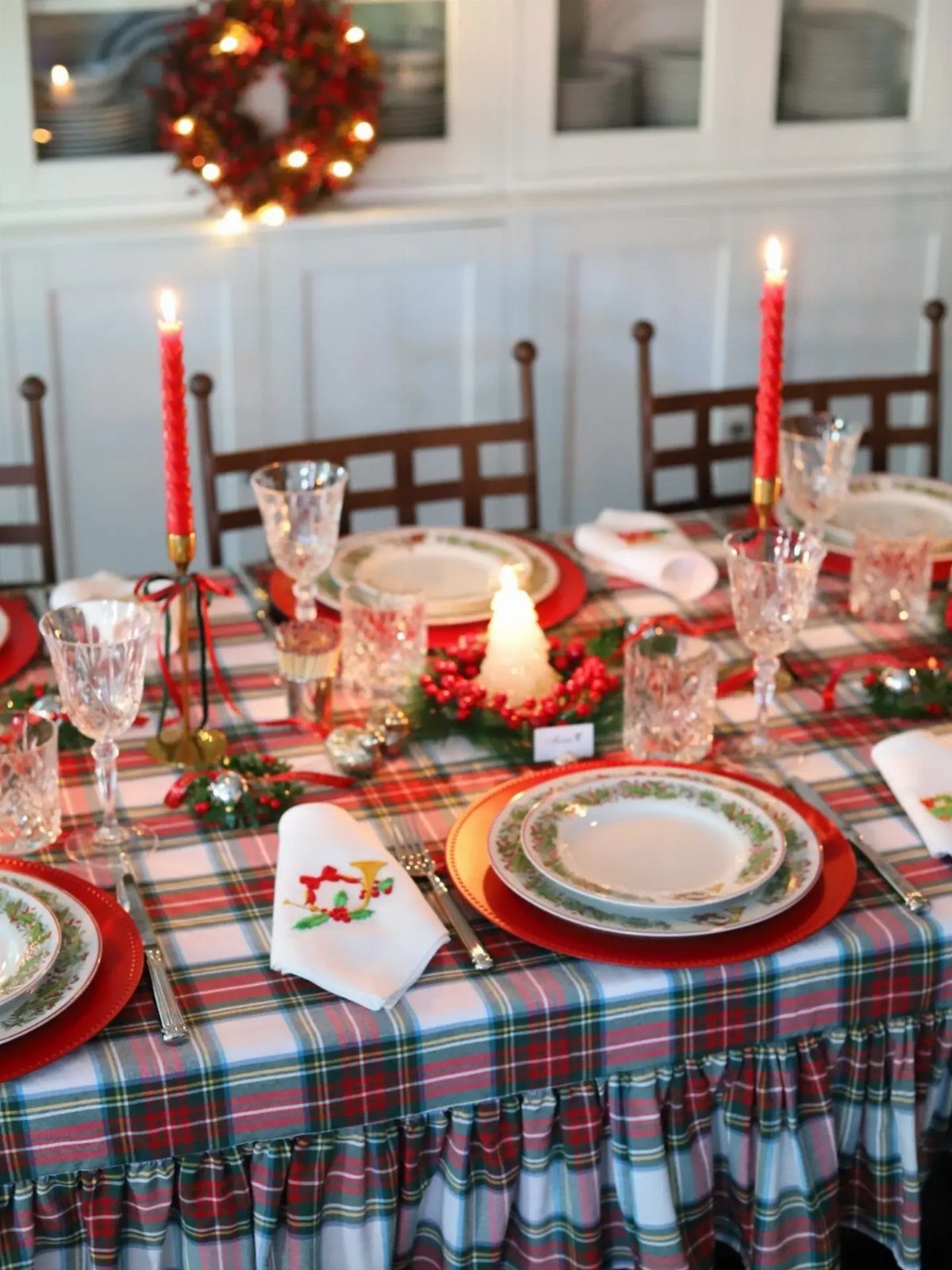 Plaid tablecloth on a Christmas dinner table with red chargers and candles.
