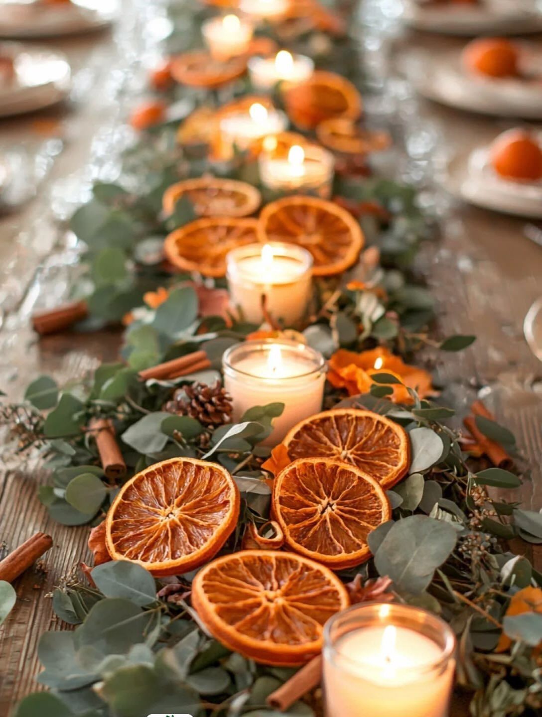 Dried orange slices and lit candles nestled in eucalyptus greenery on a wooden table.