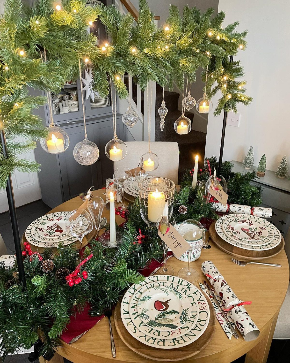 Festive Christmas table setting with a greenery arch featuring warm twinkle lights.