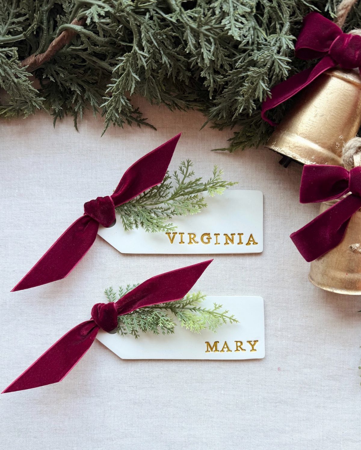 White place cards with gold names, burgundy velvet bows, and cedar sprigs.