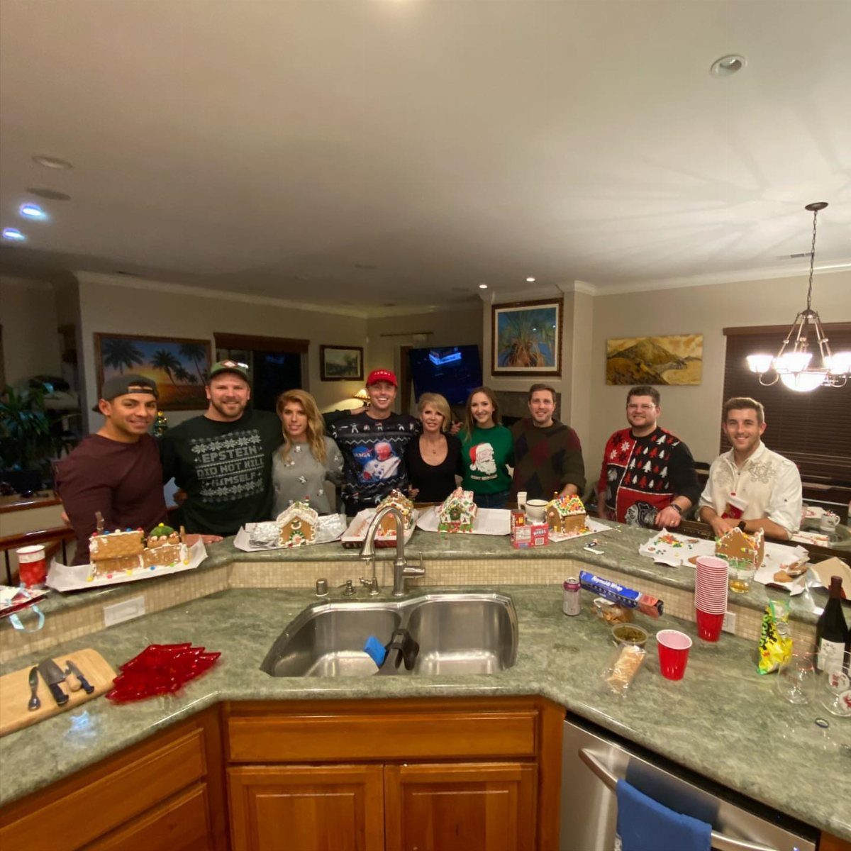 Group of adults standing behind a kitchen counter with decorated gingerbread houses.