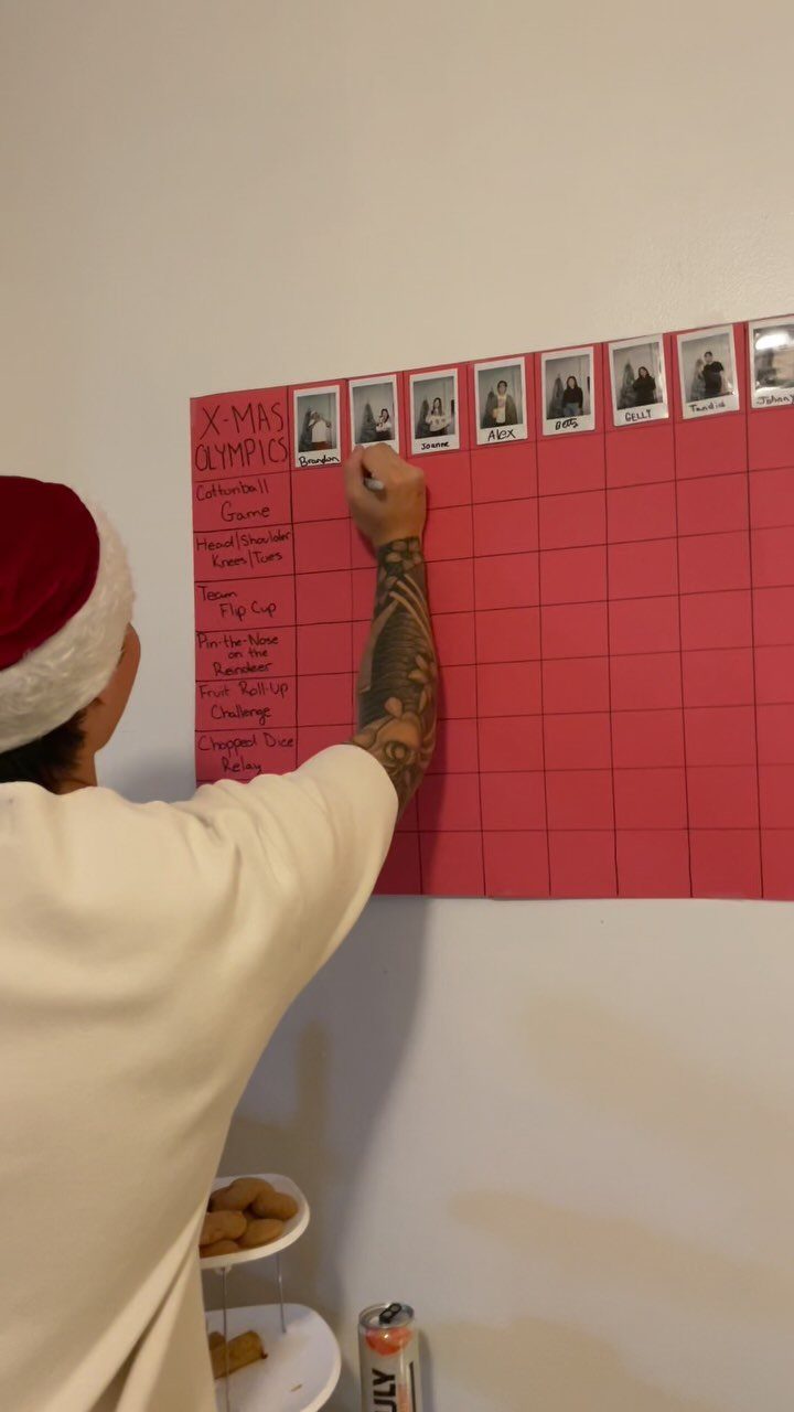 Person in Santa hat writing on a red Christmas Olympics game scoreboard chart