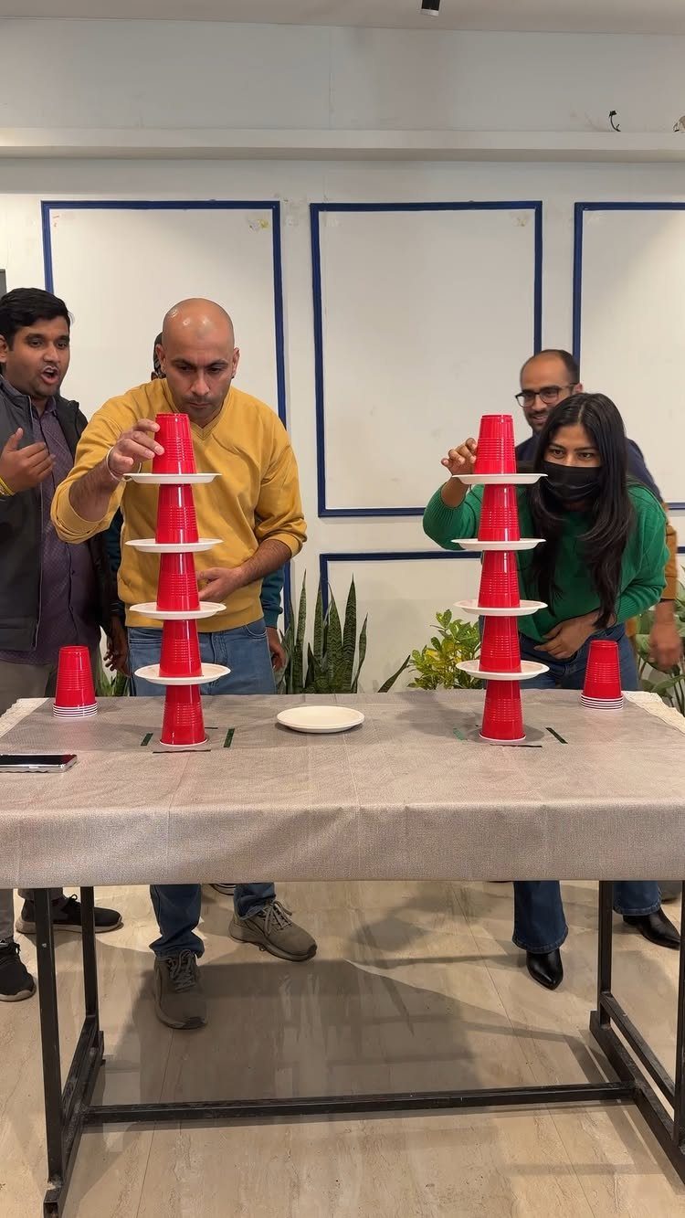 Adults competing in a red plastic cup stacking game on a grey table