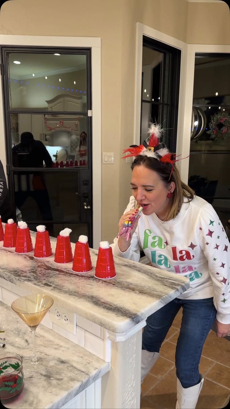 Woman in Christmas sweater playing holiday drink pong with red cups on marble counter