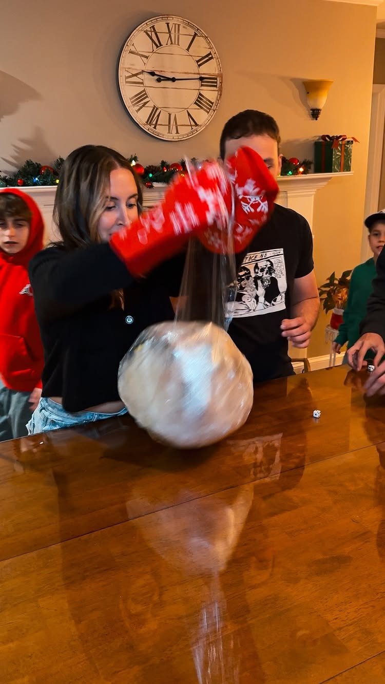 Woman wearing red oven mitts unwrapping a plastic wrap ball on a table