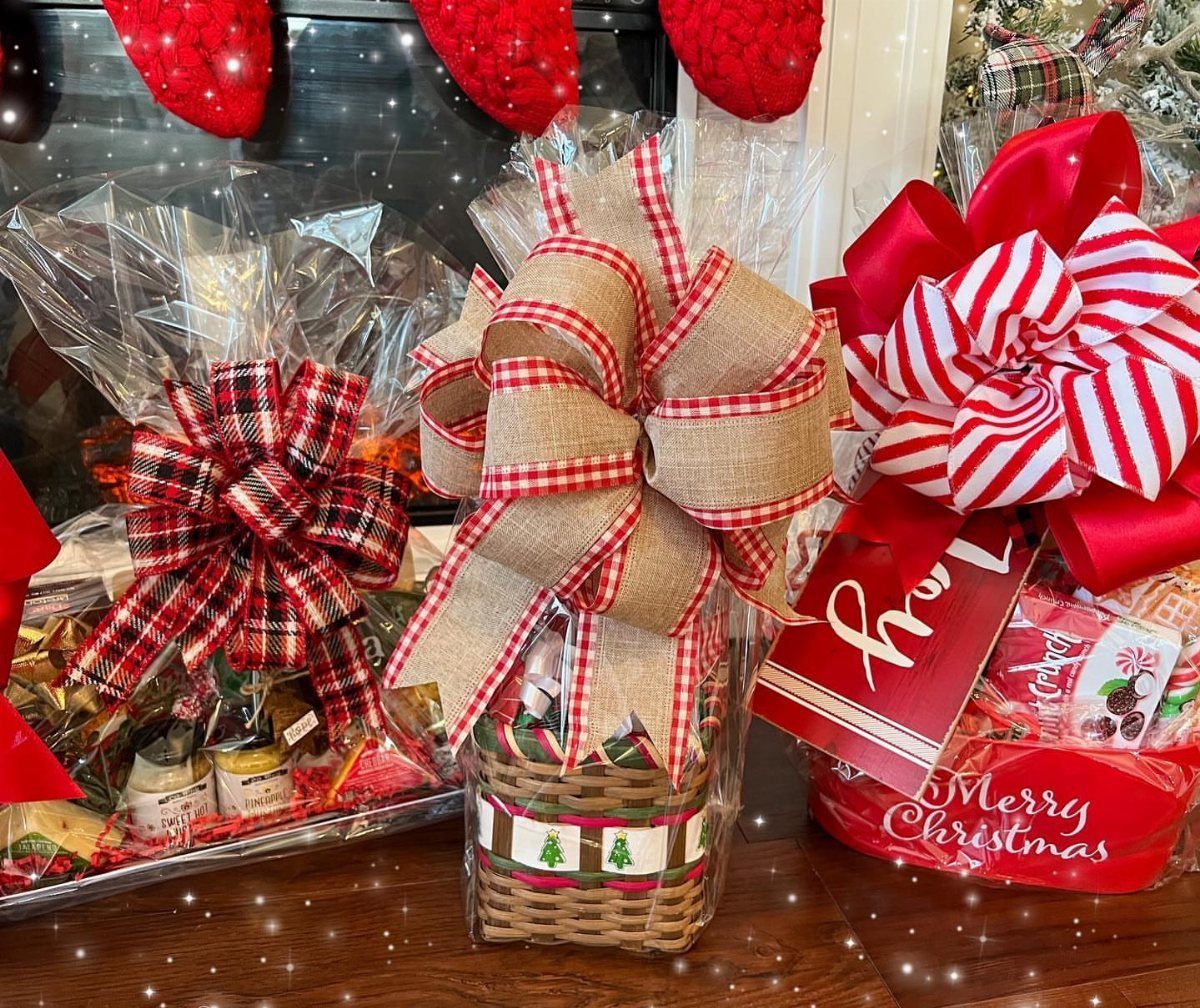 Three wrapped Christmas gift baskets with large red bows on a wooden table.