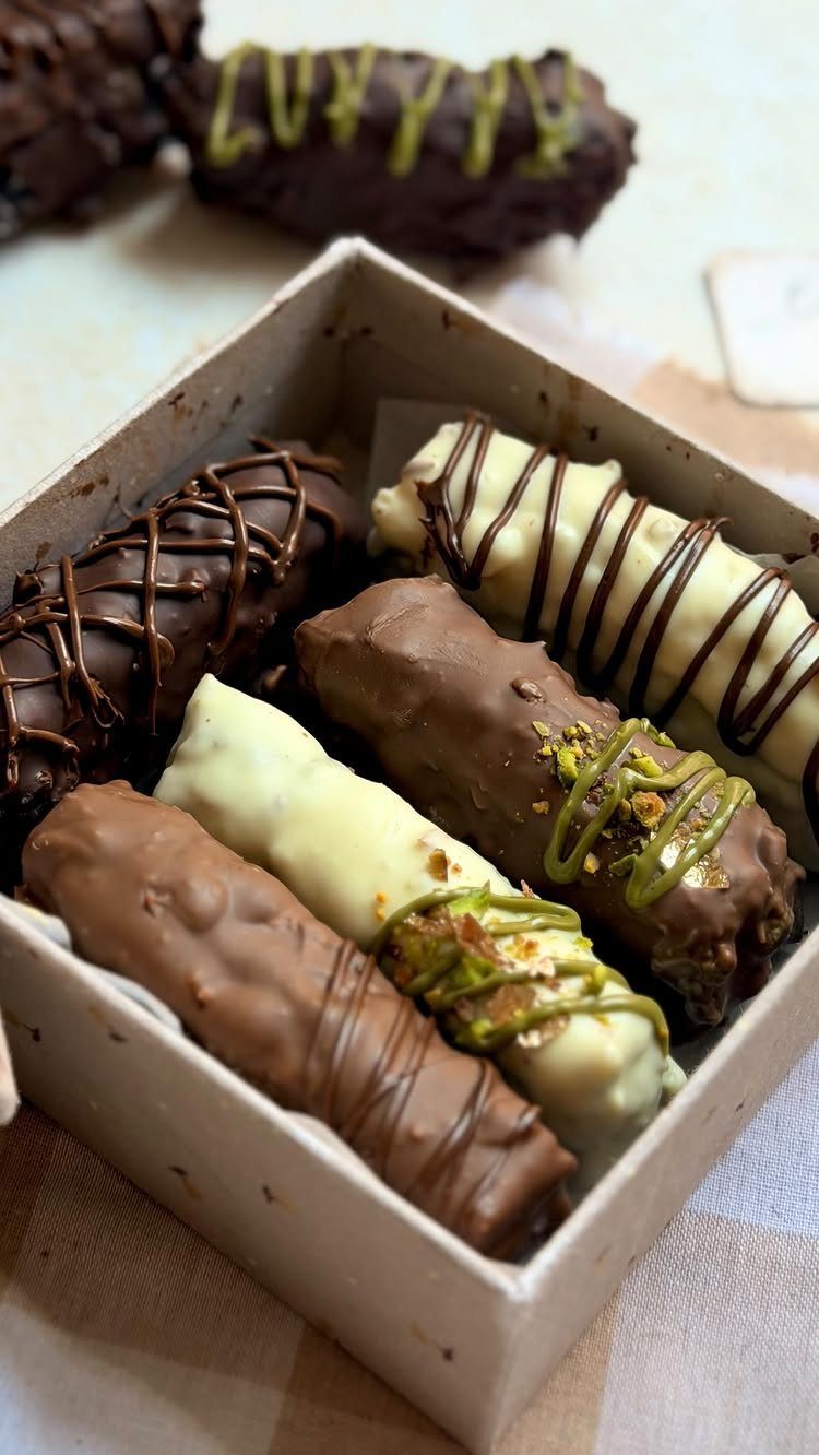 Chocolate covered treats with pistachio toppings arranged in a small cardboard gift box.
