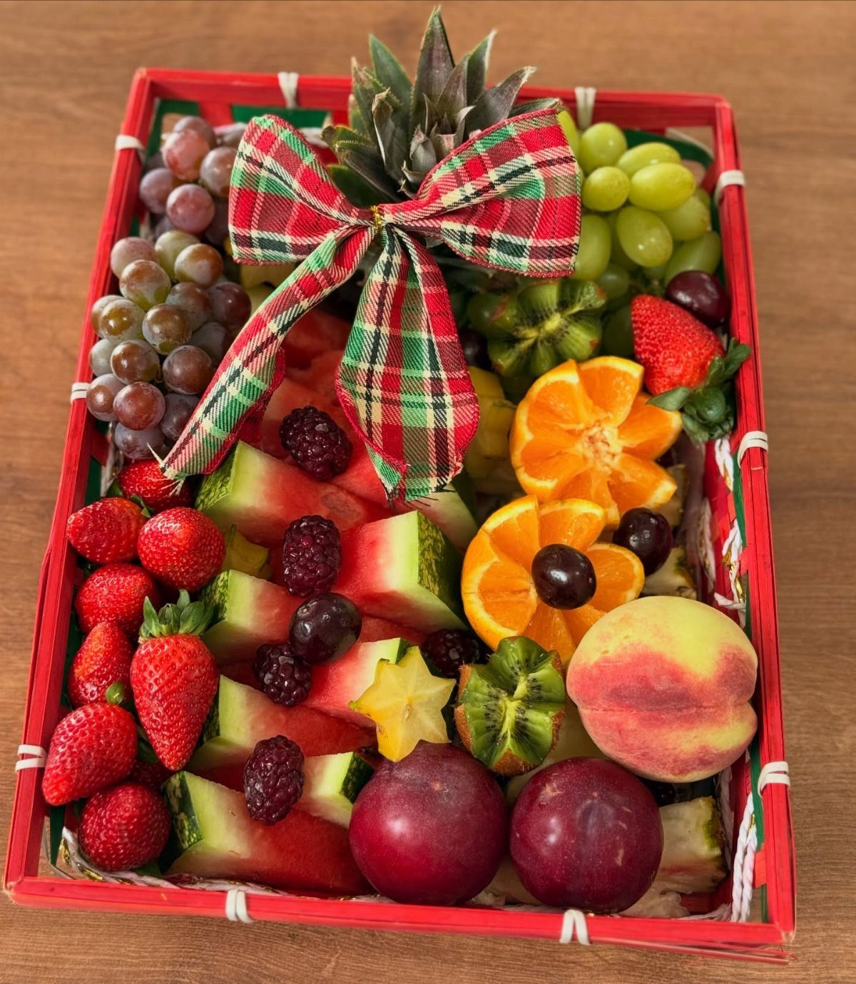 Fruit basket with strawberries, grapes, and watermelon tied with a plaid holiday bow.