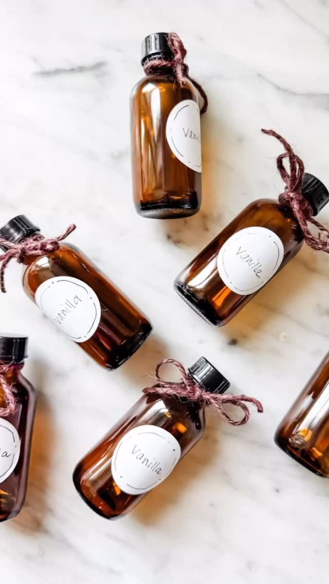 Amber glass bottles of homemade vanilla extract with twine bows on marble surface