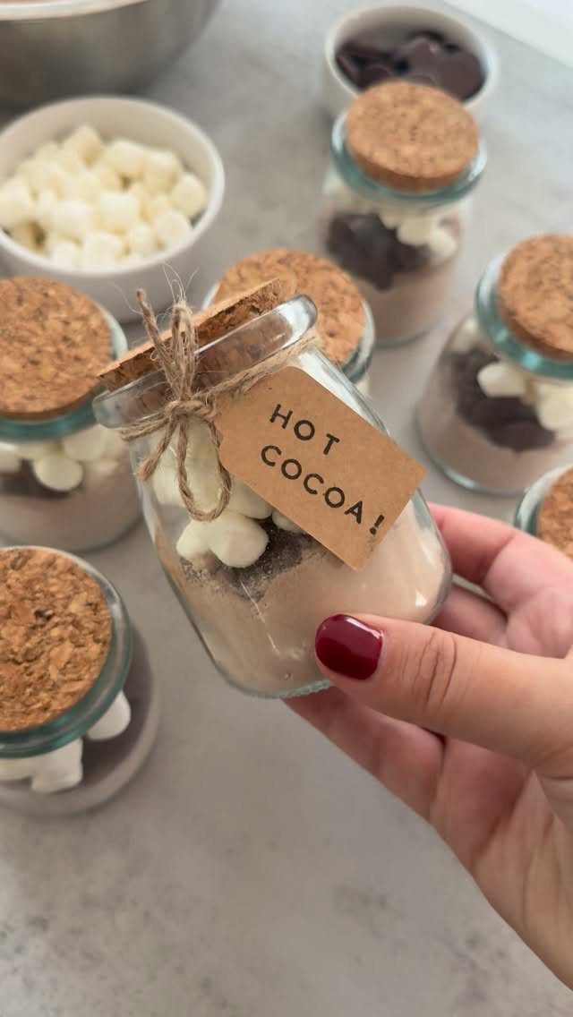 Glass jars filled with layered cocoa powder and marshmallows for hot chocolate kits.