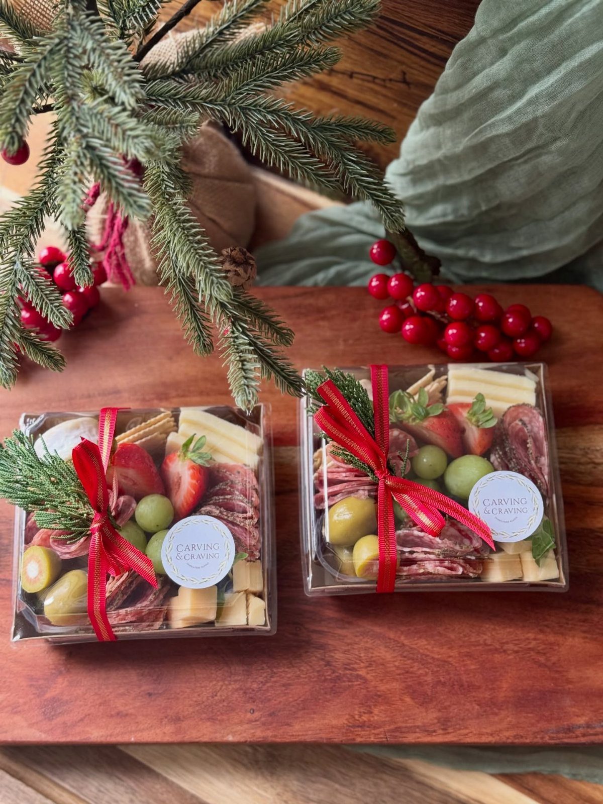 Two mini charcuterie boxes with meats, cheeses, and fruit tied with red ribbons.