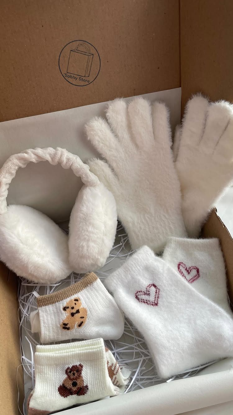 White fuzzy gloves, earmuffs, and patterned socks arranged in a cardboard gift box.