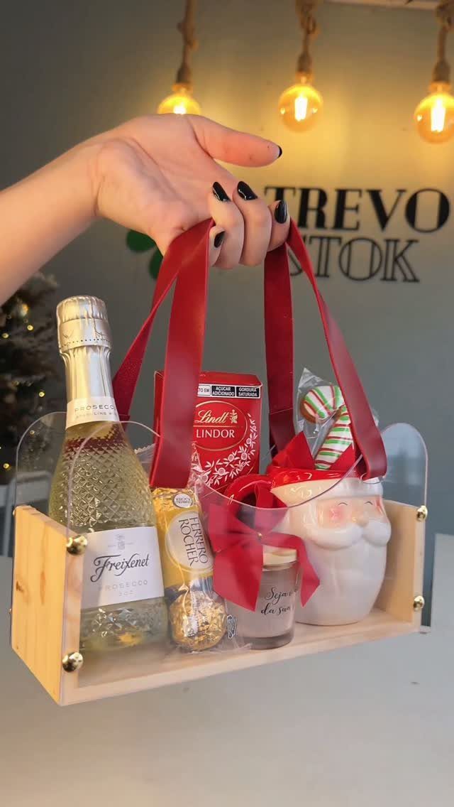 Wooden gift tray with sparkling wine, chocolates, and Santa mug held by red ribbons