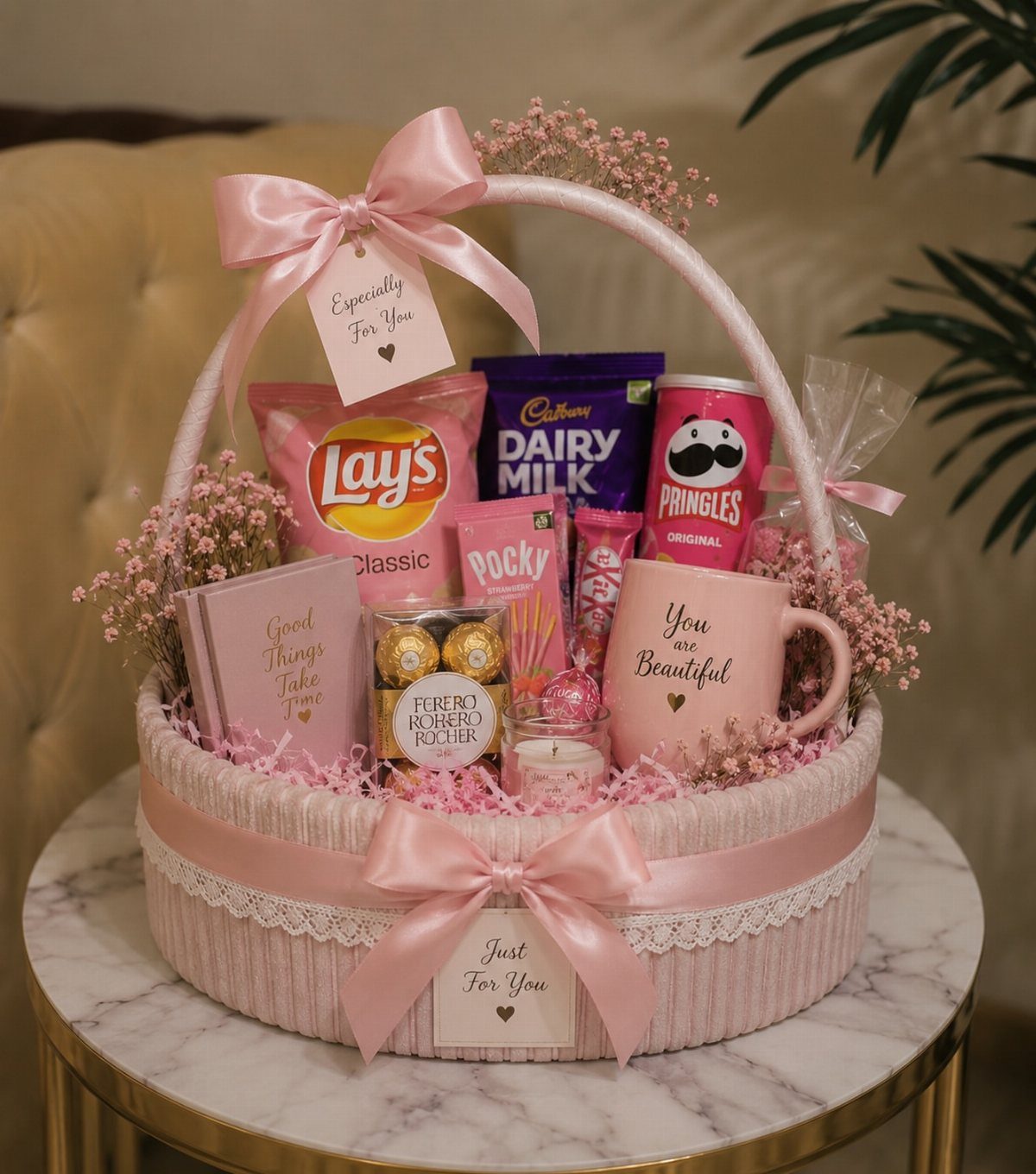 Pink gift basket filled with snacks, chocolates, and a mug on marble table