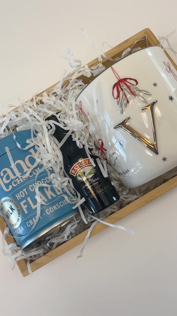 Hot chocolate gift basket with a blue tin, syrup, and white ceramic mug.