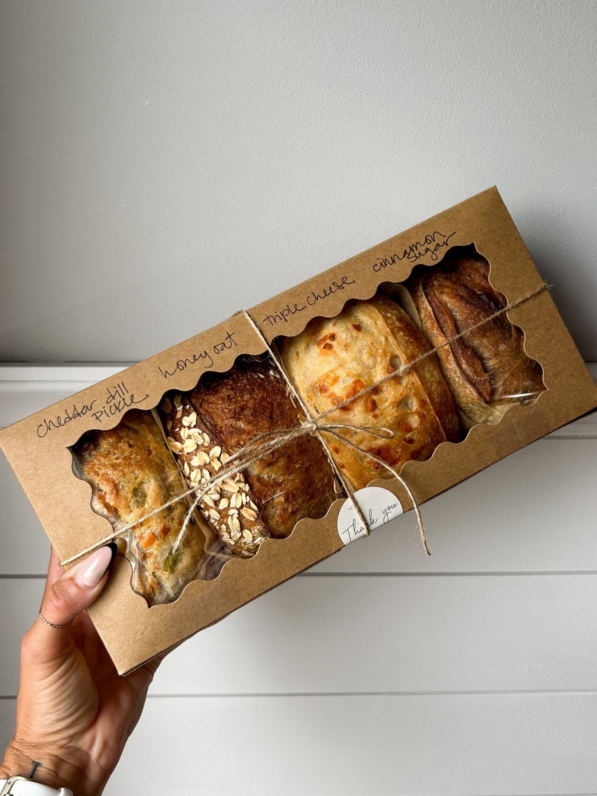Assorted artisanal bread loaves in a brown cardboard gift box tied with twine.