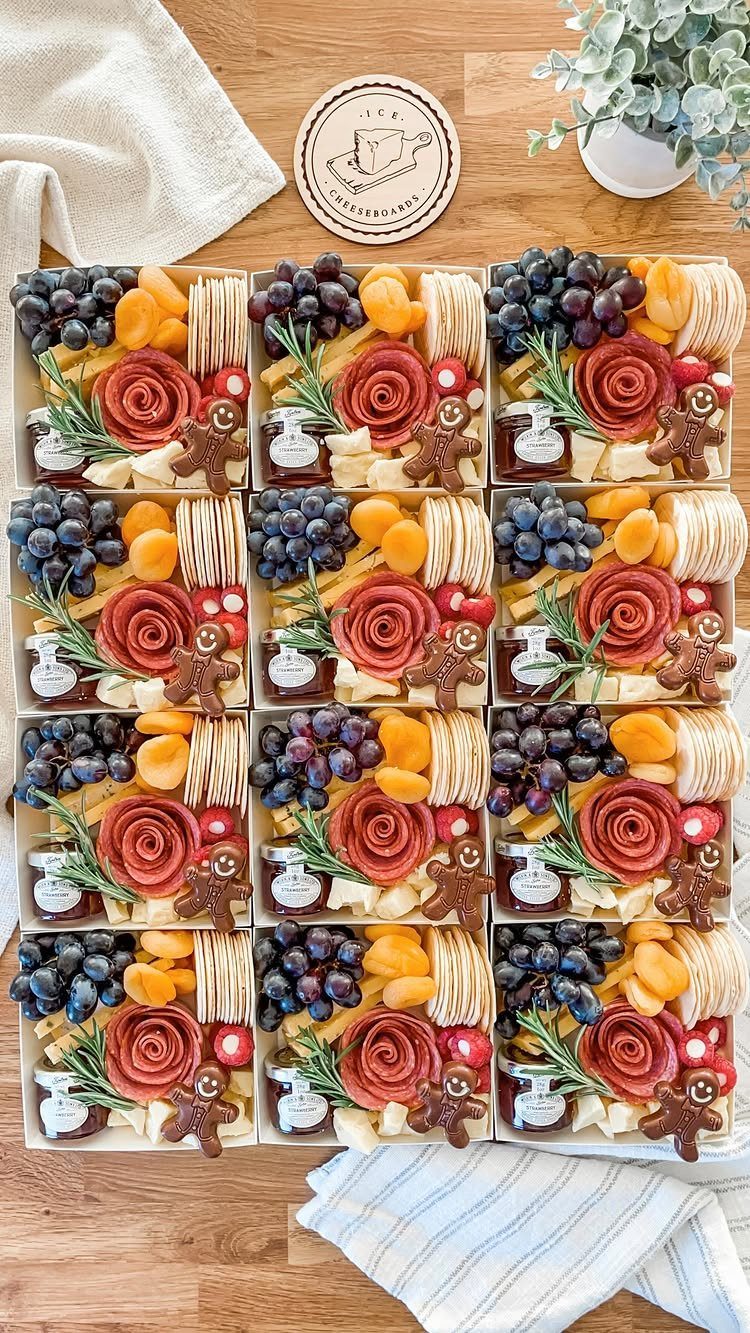 Twelve charcuterie gift boxes with meats, cheeses, fruits, and gingerbread men on wood.