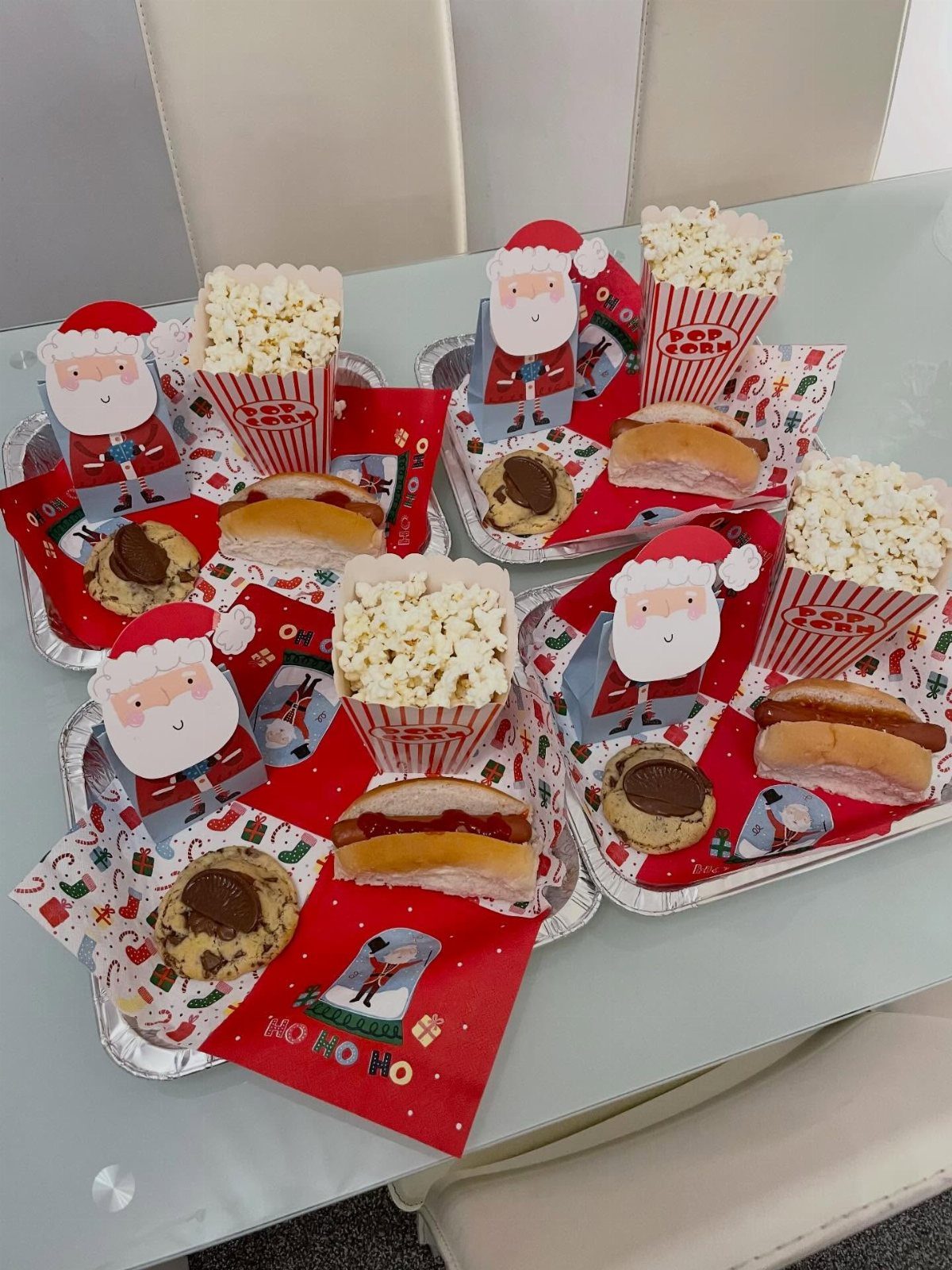 Four Christmas snack trays with burgers, cookies, popcorn, and Santa decorations on a table