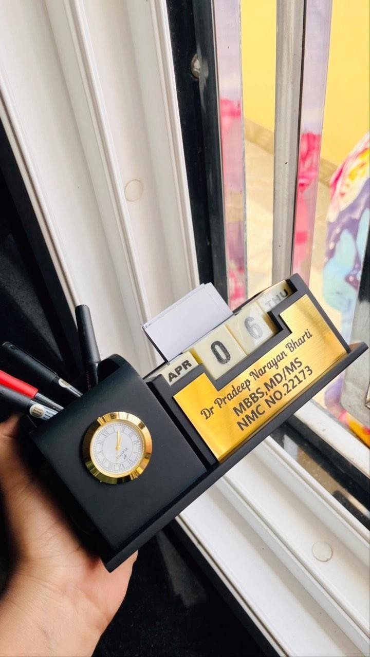 Black desk organizer with clock, calendar, and gold nameplate held by a hand.