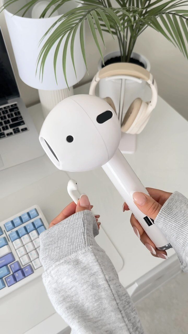 White wireless earbuds and charging case held over a clean white office desk.